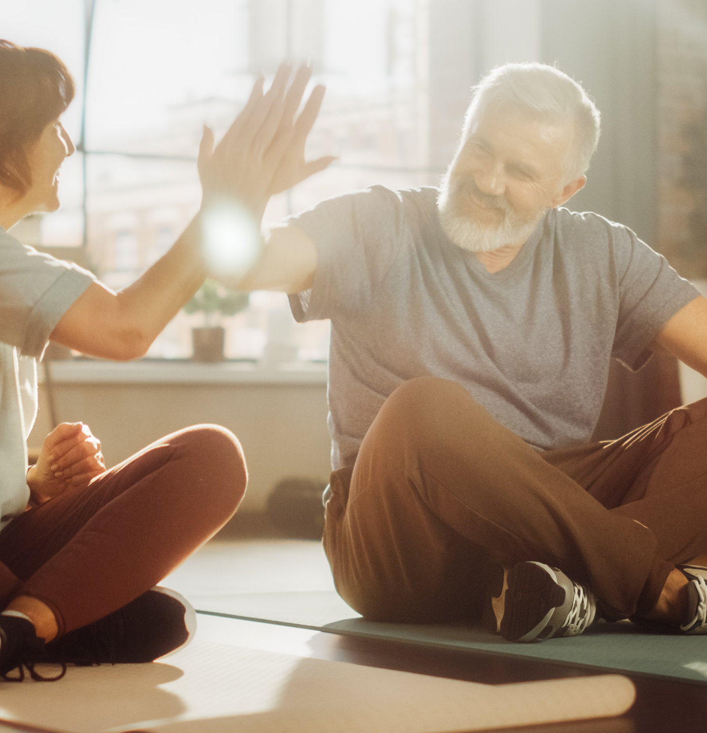 Eine Frau (links) und ein Mann (rechts) sitzen auf dem Boden im Schneidersitz mit Sportkleidung und geben sich einen Handschlag